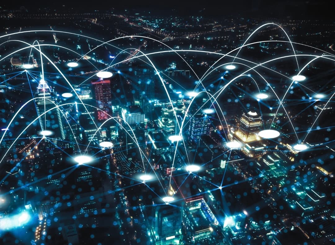 A futuristic cityscape at night with glowing white network lines and nodes connecting various buildings, symbolizing global digital connectivity.