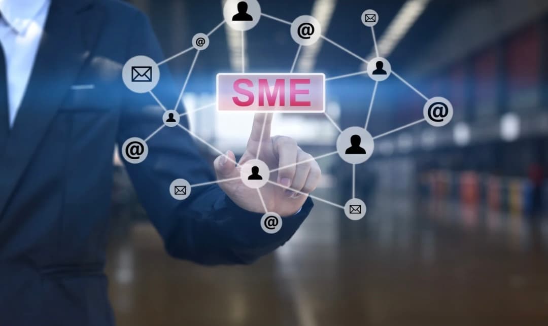 A business professional in a suit pointing at a digital screen with the word "SME" (Small and Medium Enterprise) at the center, surrounded by network icons such as email, people, and communication symbols.